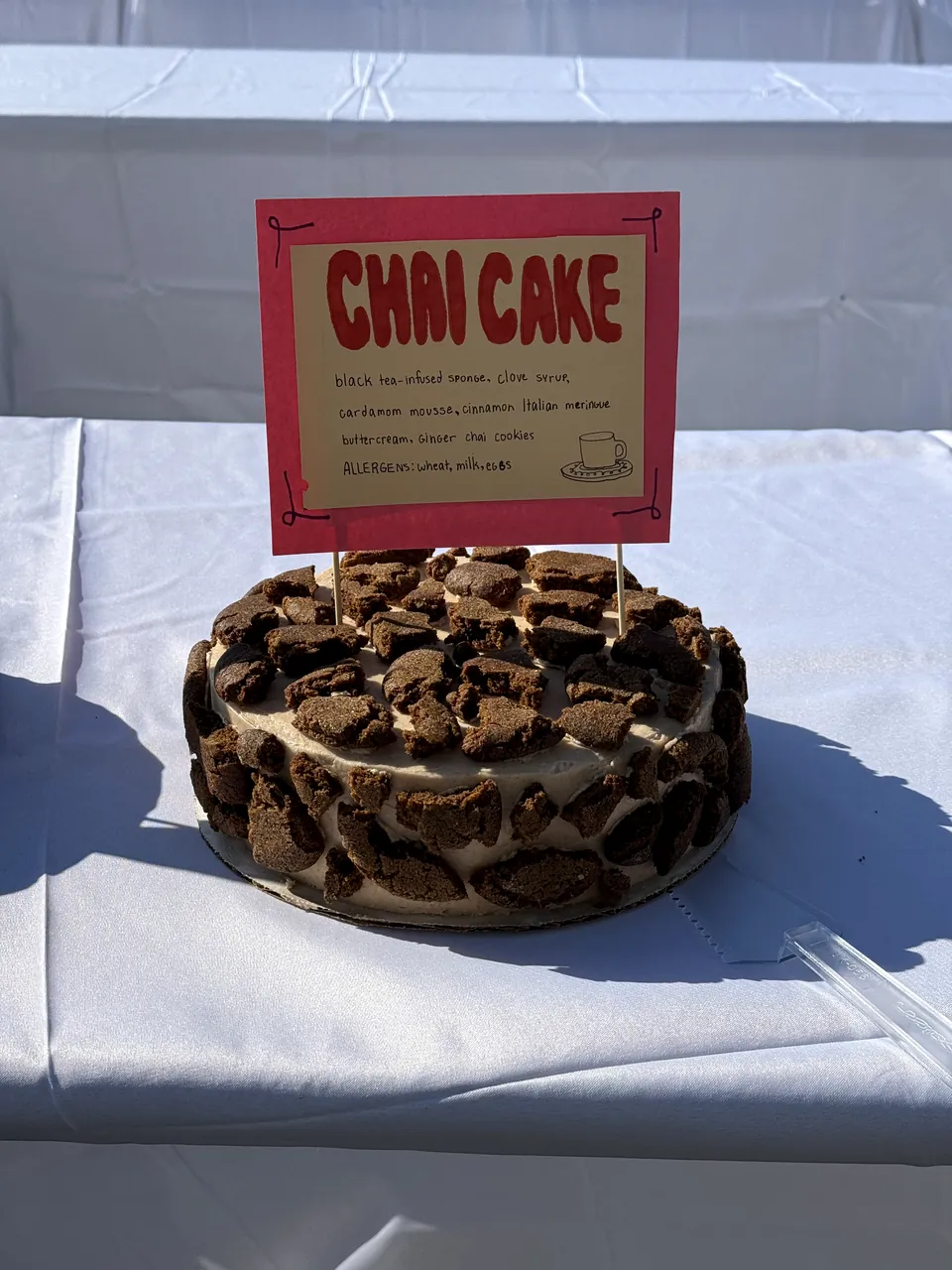 Chai cake finished with cookie pieces, with its hand-lettered sign